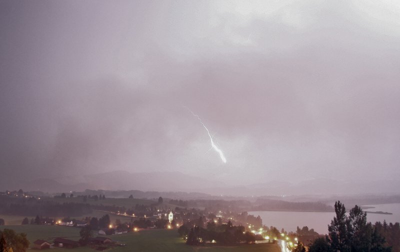 Heftiger Blitzeinschlag während einem Gewitter hinter Hopfen am See bei Nacht. 